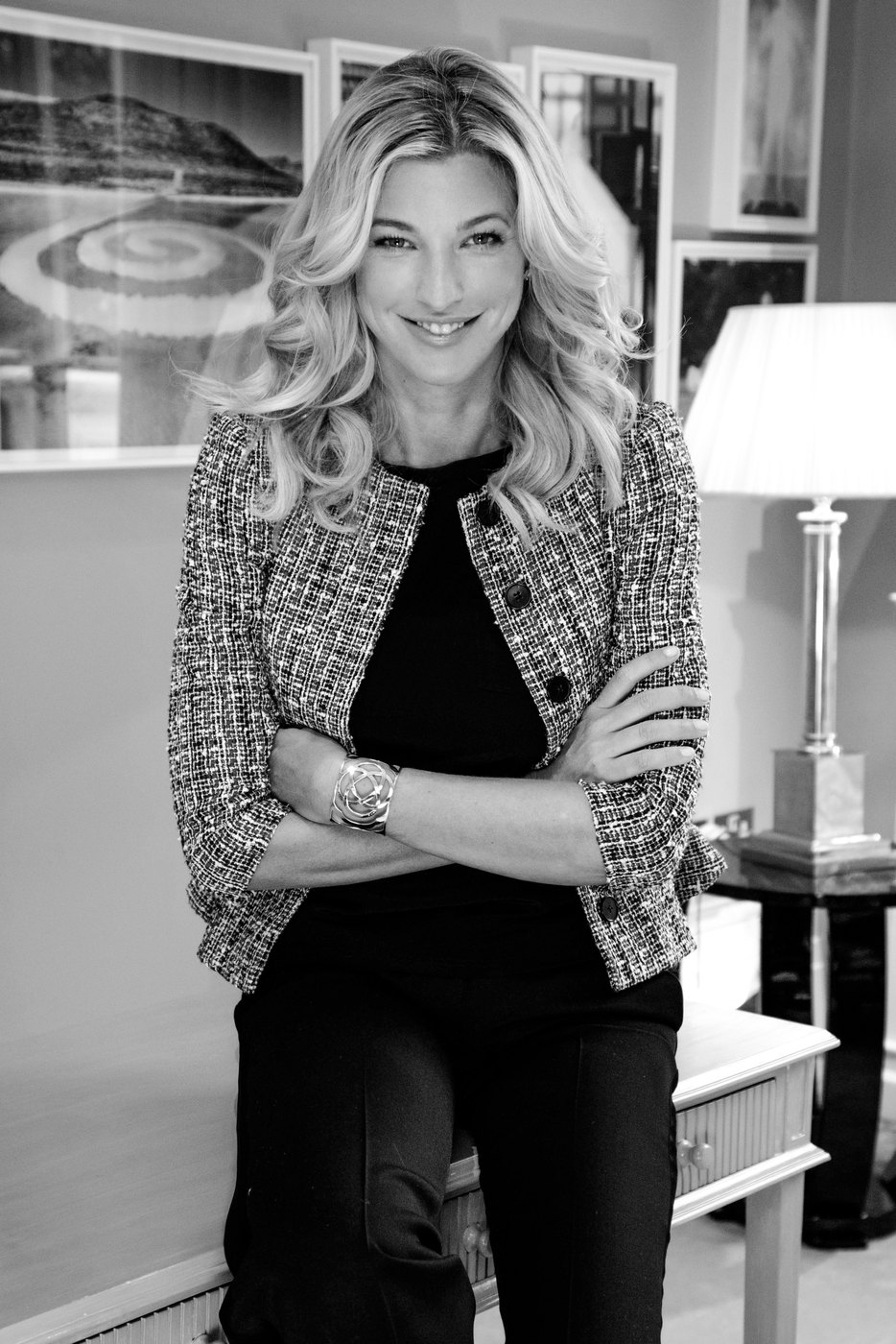 Nicole Junkermann in a black and white editorial portrait, standing in a light room with framed pictures behind her
