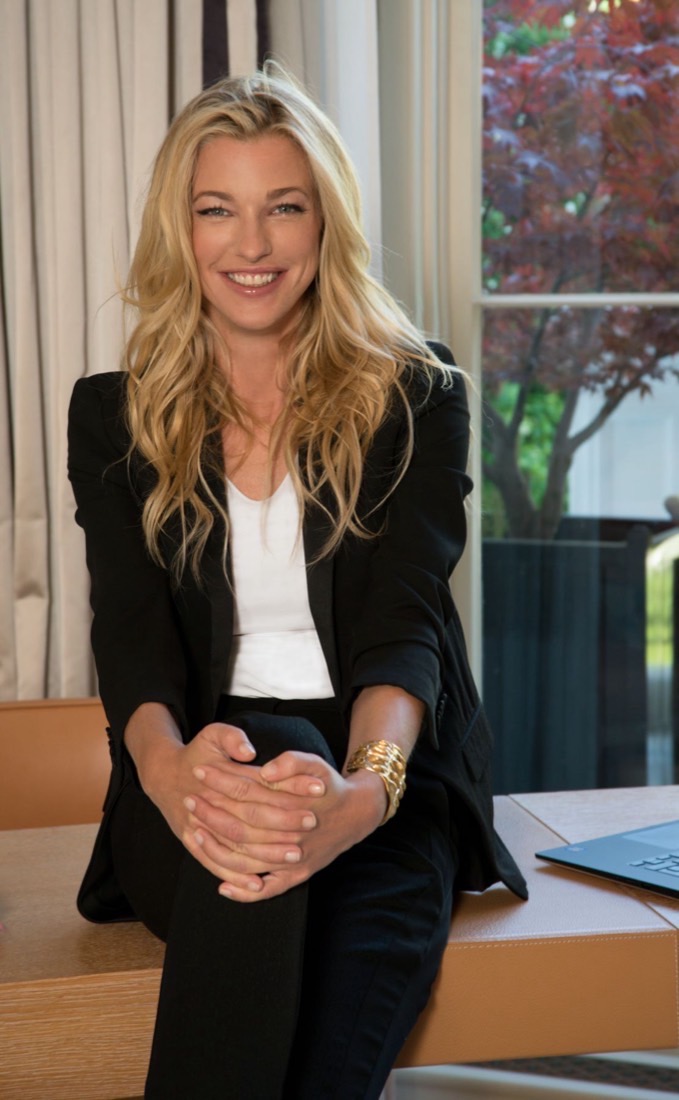 Nicole Junkermann in a black blazer, smiling warmly, seated by a bright window