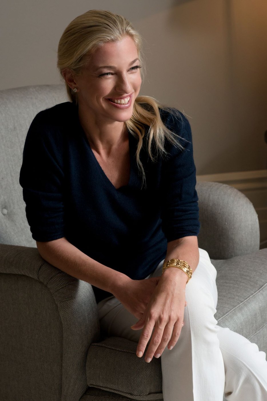 Nicole Junkermann seated on a pale sofa in a warm interior, smiling in conversation